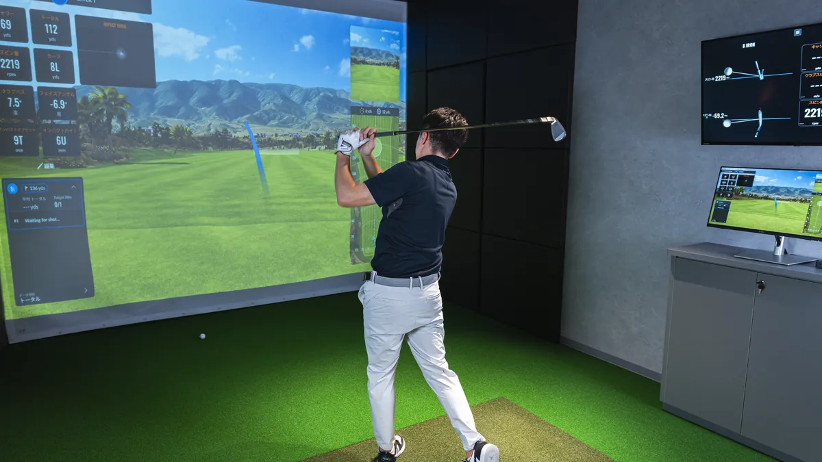 T-One Golf Studioの打席でTrackManのデータを見ながらスイングするゴルファー