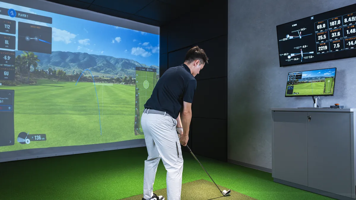 T-One Golf Studioの打席でアイアンを構えるゴルファー 奥のモニターにTrackManのデータが表示されている