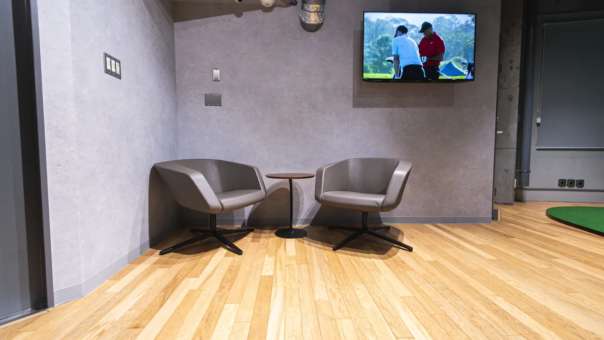 T-One Golf Studioの休憩スペース 椅子2脚と小さなテーブル、壁にテレビ
