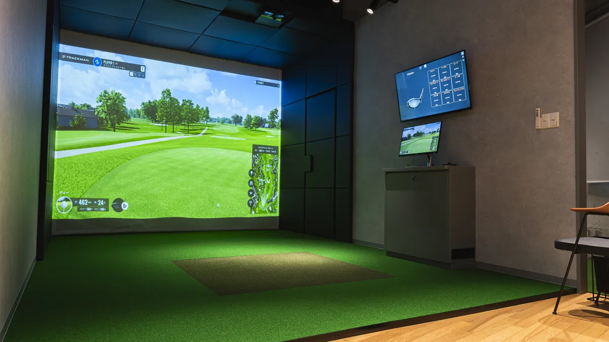 T-One Golf Studioの暖かい室内の打席 スクリーンにゴルフコースが映っている