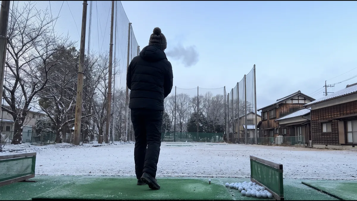 冬の早朝の屋外ゴルフ練習場 雪の残る打席と厚着のゴルファーの後ろ姿